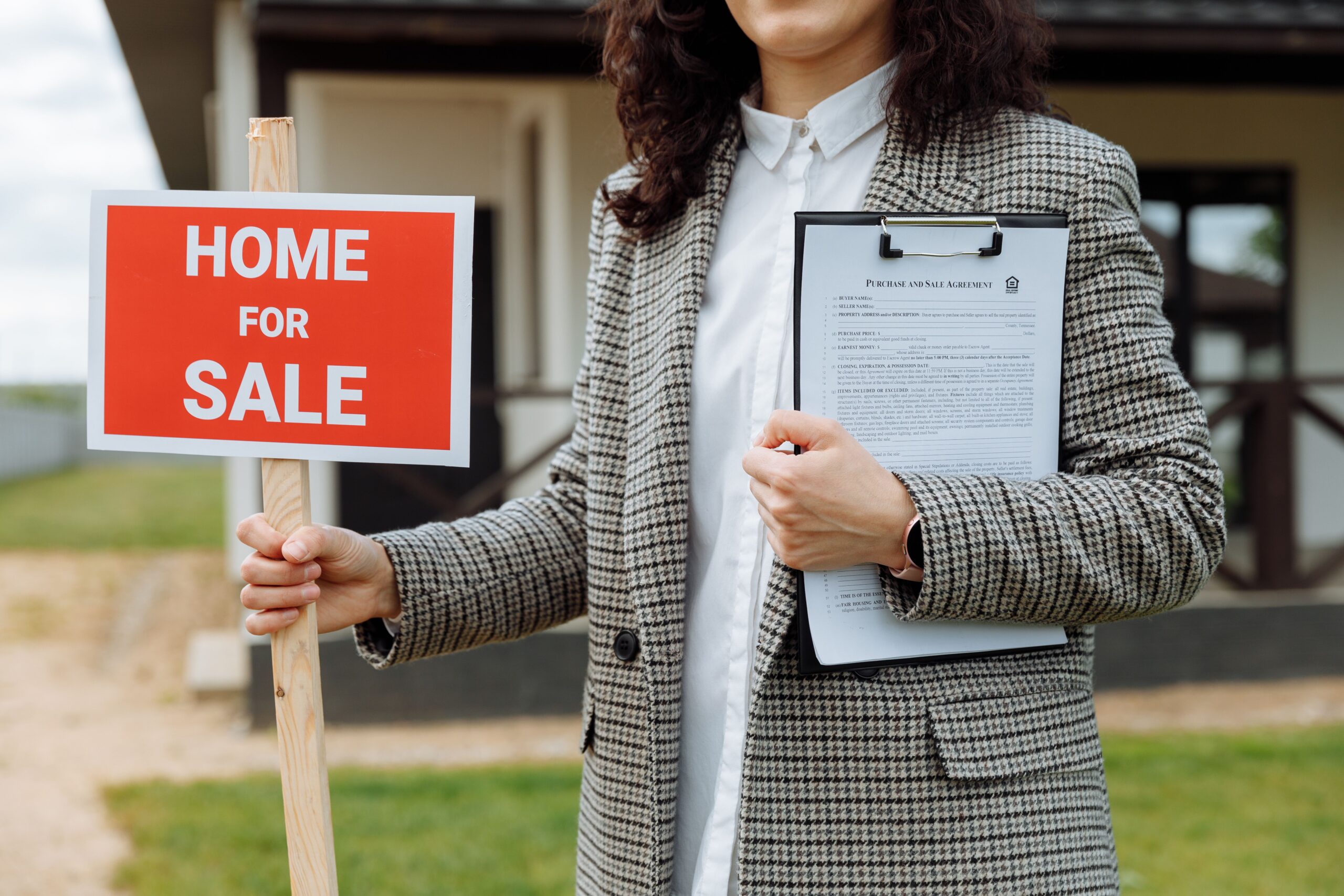 hero image of an agent holding a "home for sale" sign, while standing outside of the home she's selling